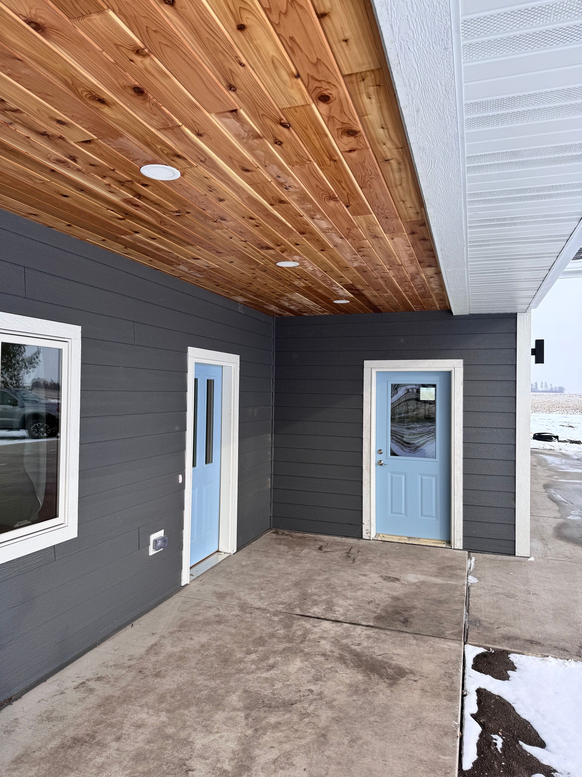 Covered porch with gray siding, light blue doors, and wood ceiling.