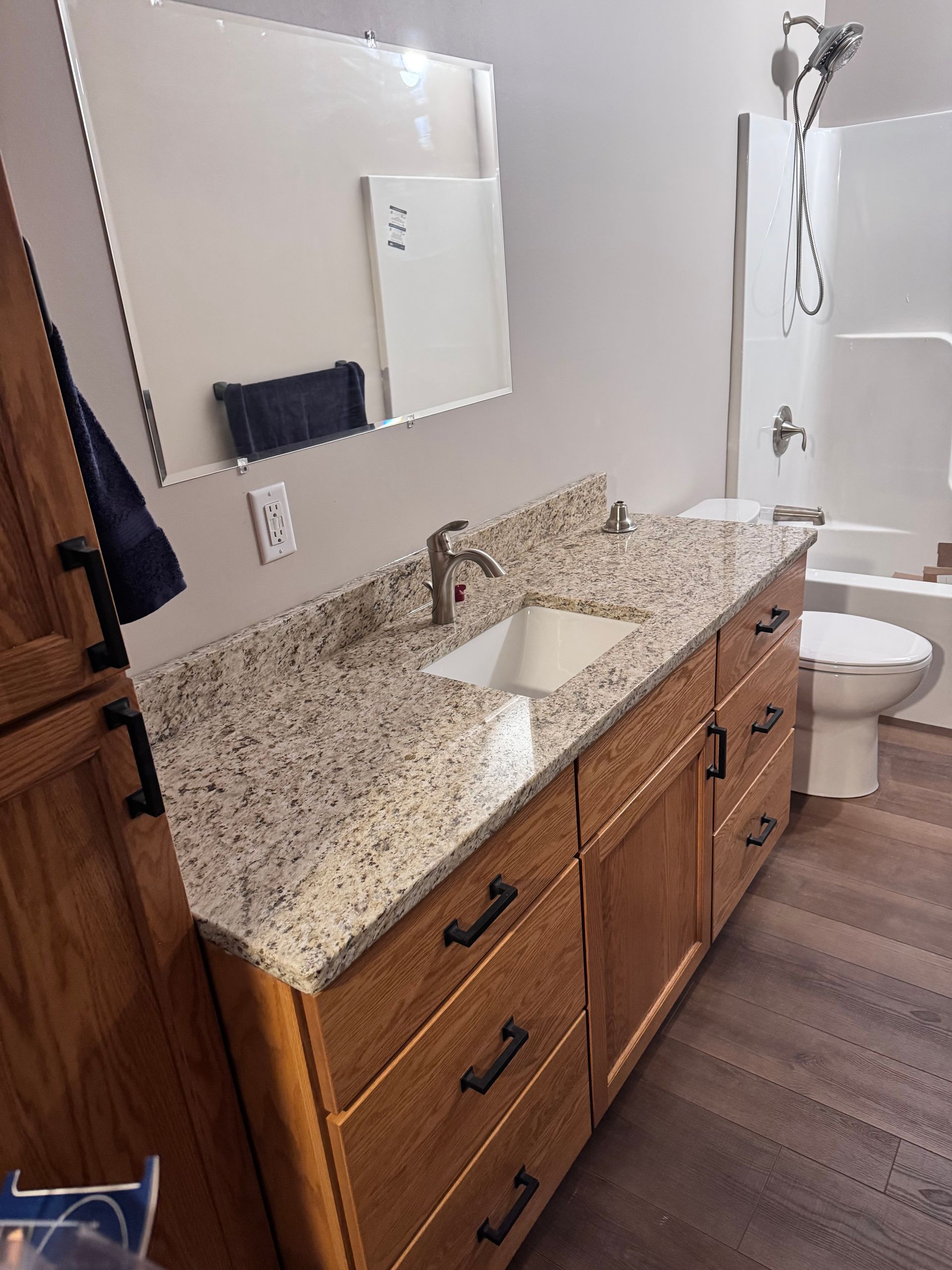 Bathroom with oak vanity, granite countertop, white sink, large mirror, and shower.