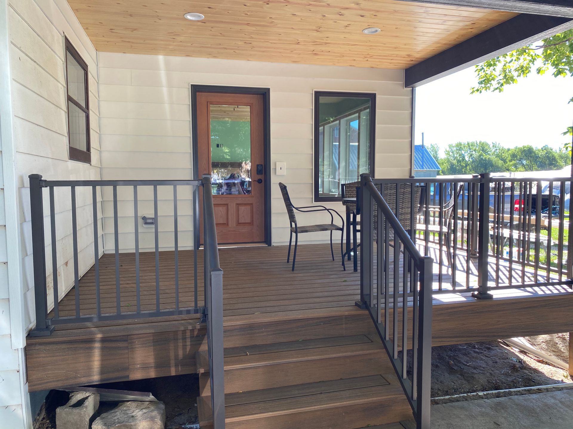 Exterior of a building with a deck and steps. Brown door, windows, and railing.  Wooden deck.