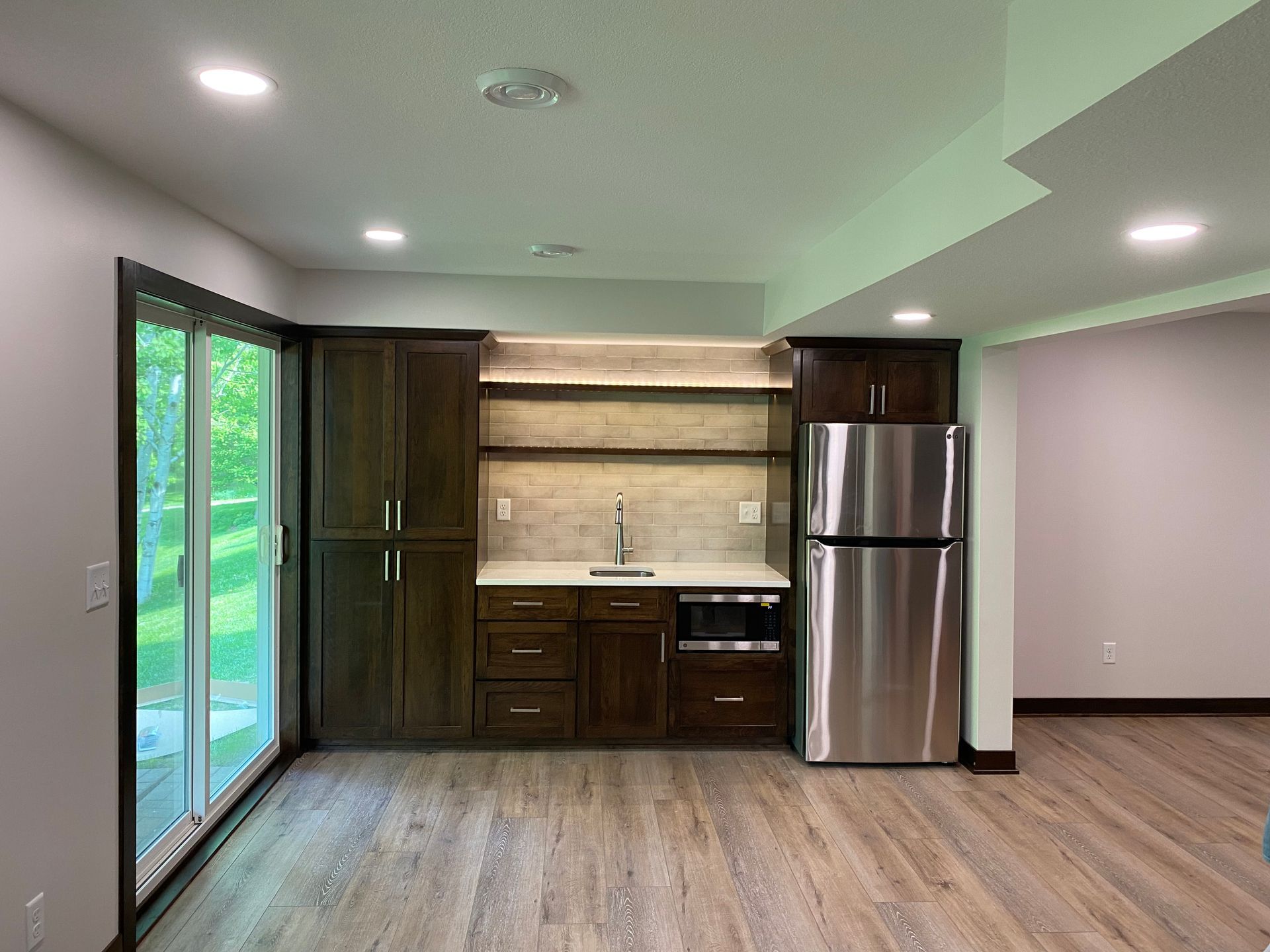 Dark brown cabinets with a sink, microwave, and refrigerator. A sliding glass door and wood-look flooring are present.