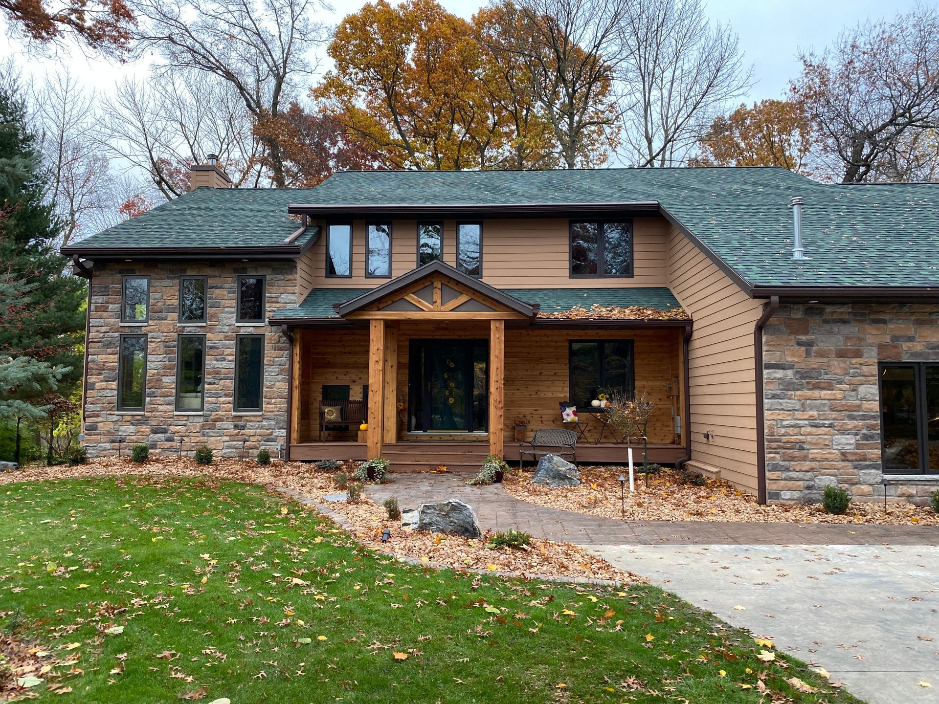 House exterior with stone facade, tan siding, green roof, wooden porch, and fall foliage.