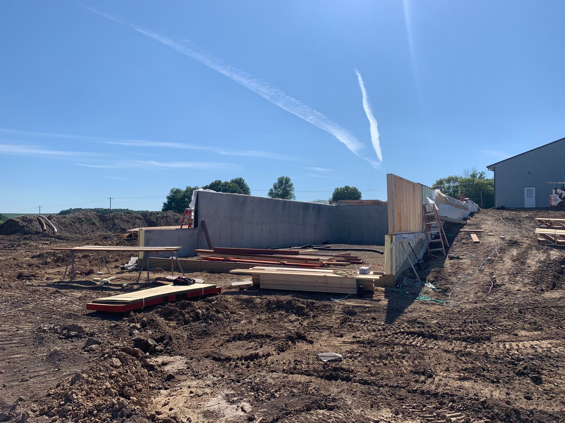 Construction site with concrete foundation, lumber, and blue sky.