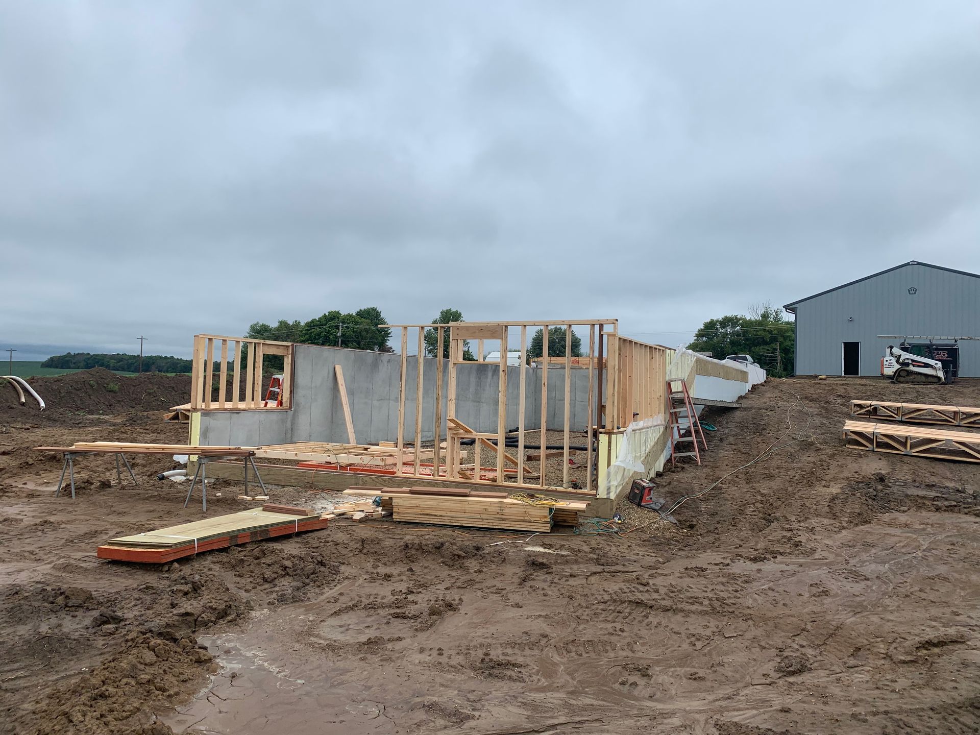 Construction site of a house. Wooden frame rising from a concrete foundation in a muddy field on a cloudy day.