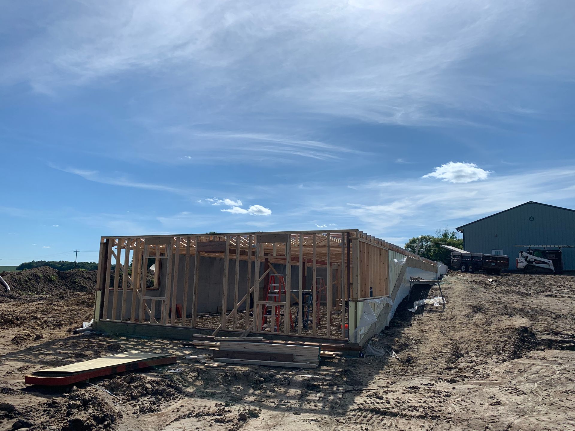 Wood frame of a building under construction on a dirt lot under a blue sky.