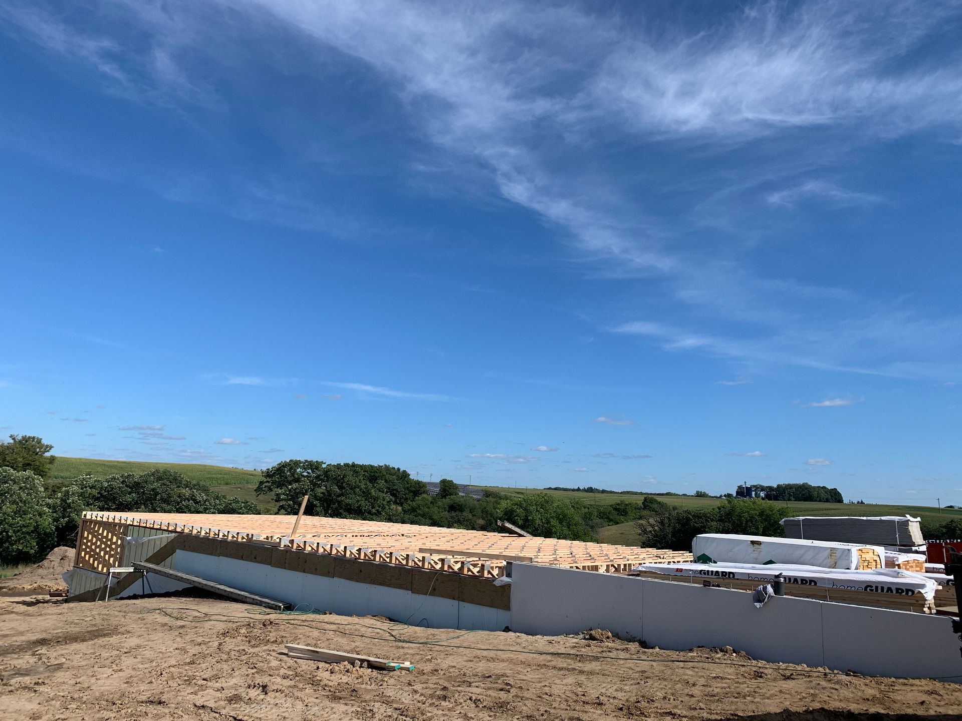 Construction site with a partially built house frame against a blue sky.
