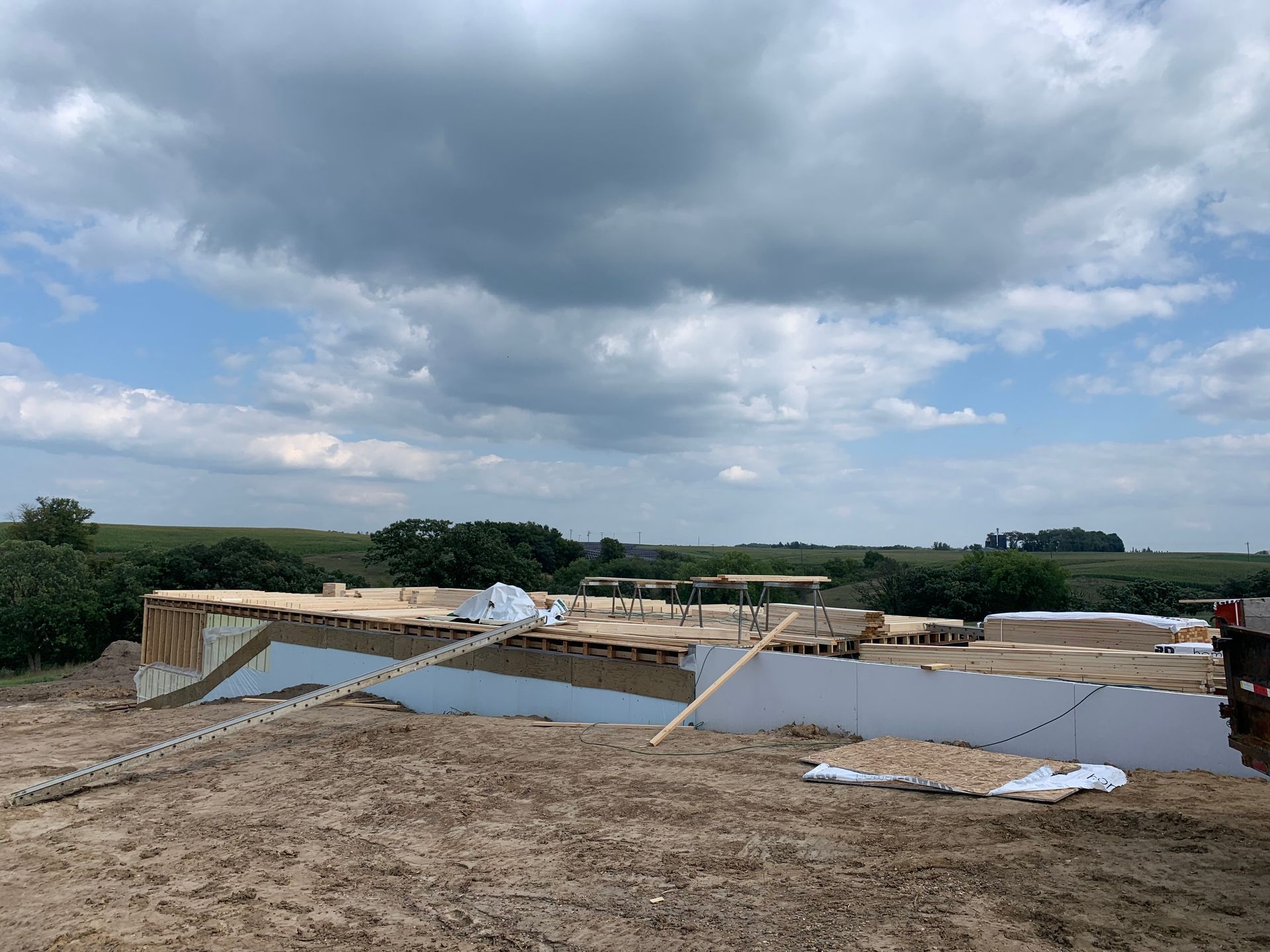 Construction site with wooden framing, surrounded by dirt, under a cloudy sky.