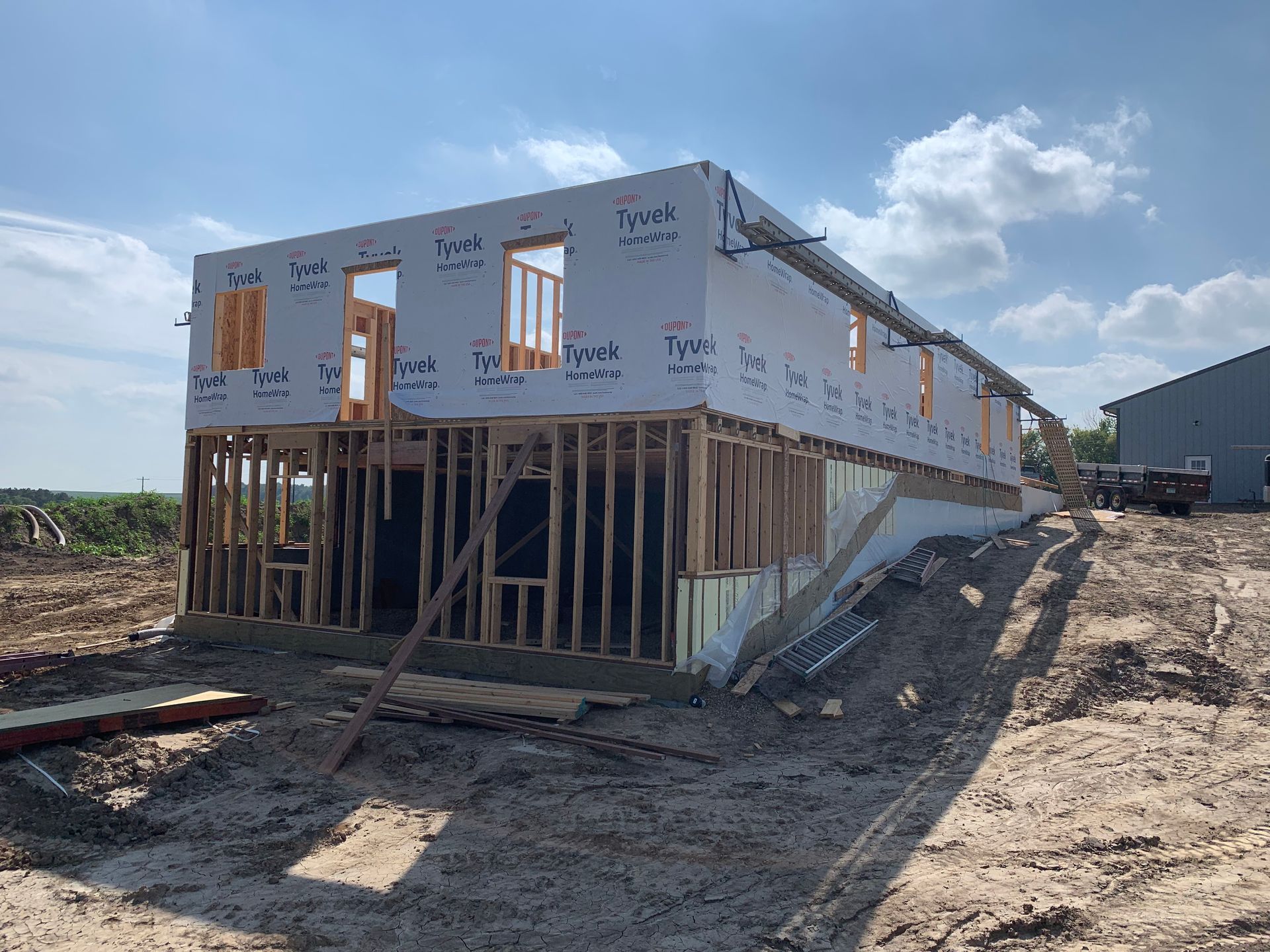 Two-story building under construction; wood framing, white siding, blue sky.