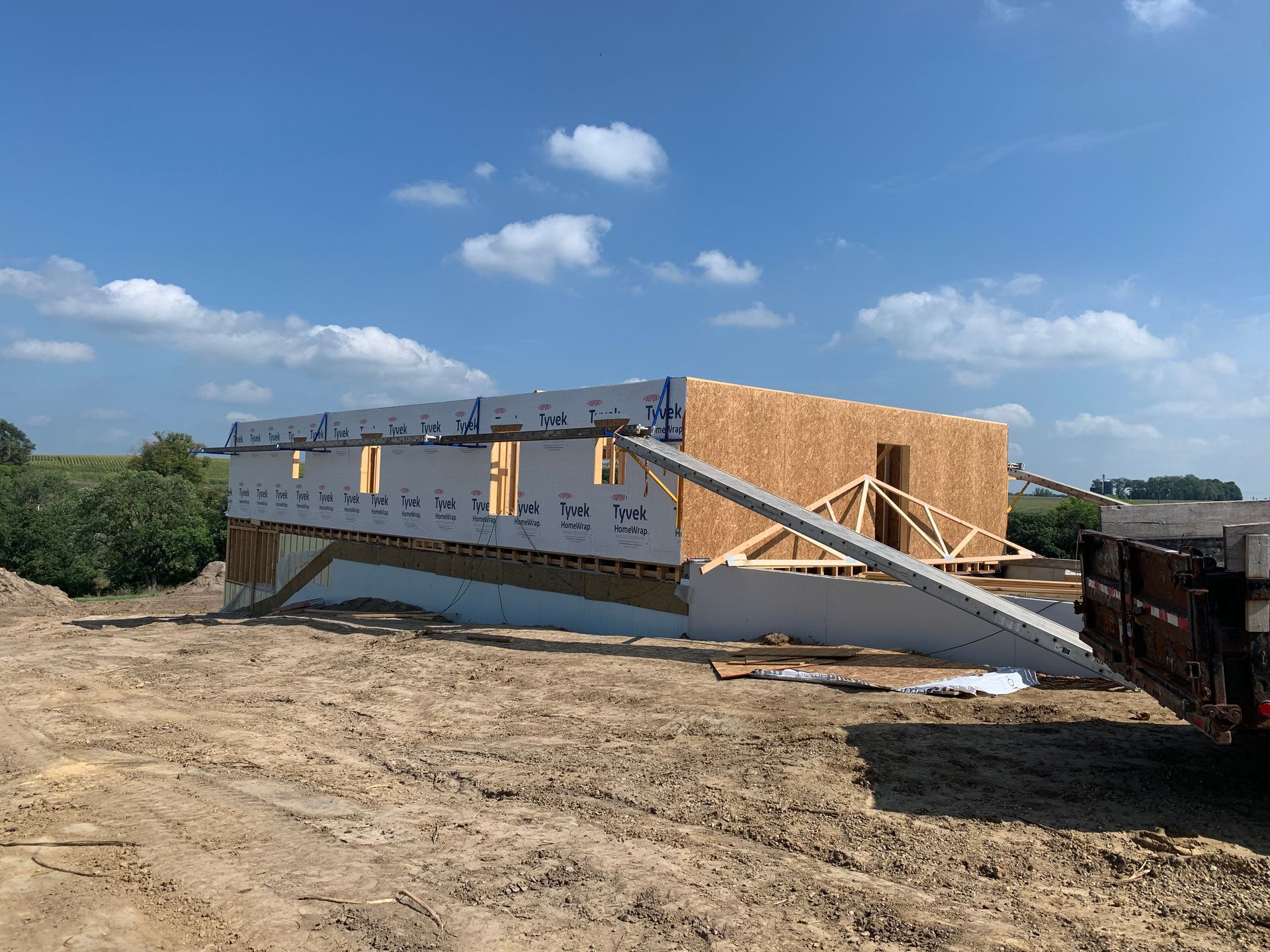 Construction site: wood-framed building on a raised foundation, blue sky, brown dirt.