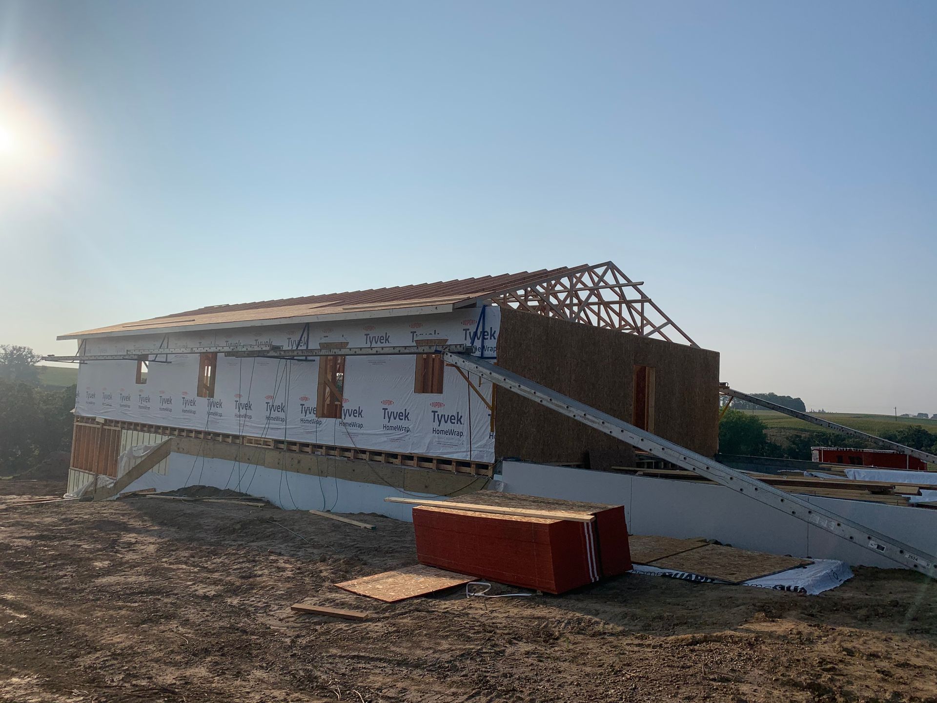 Construction site: a house frame with exposed wood and insulation, against a blue sky.
