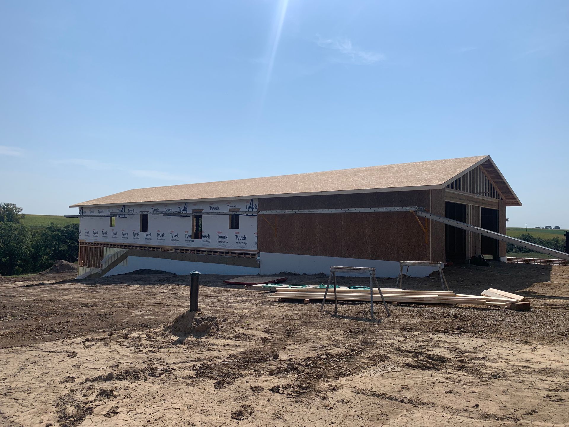 Construction of a new wood-framed building; exterior walls are covered with insulation, roof partially shingled, set in a field.