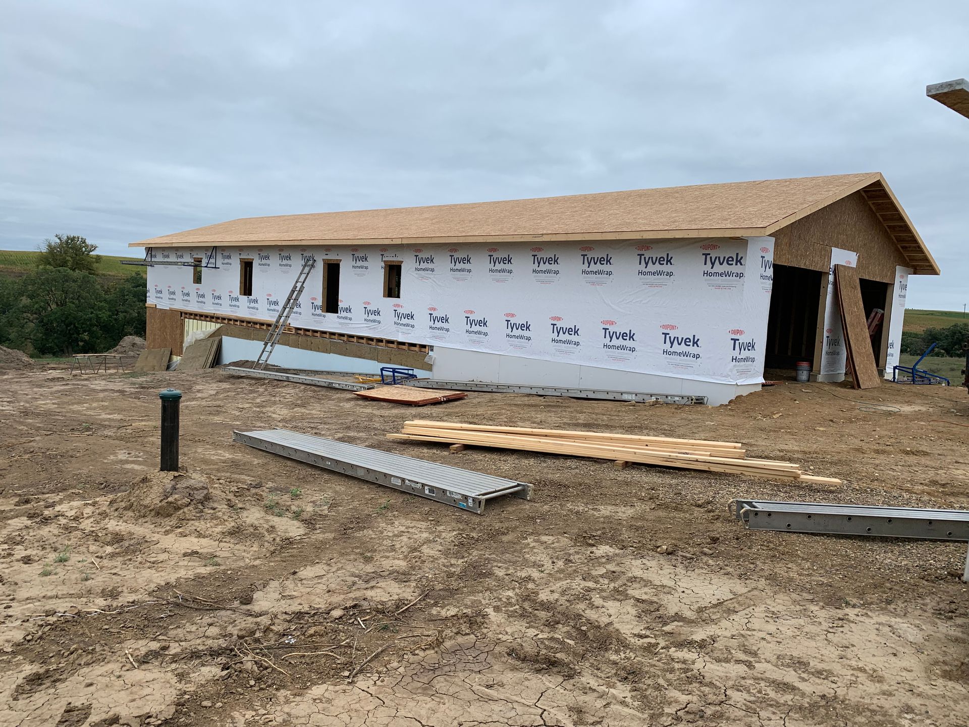 Building under construction, with plywood roof and wrapped in Tyvek, outdoors on a cloudy day.