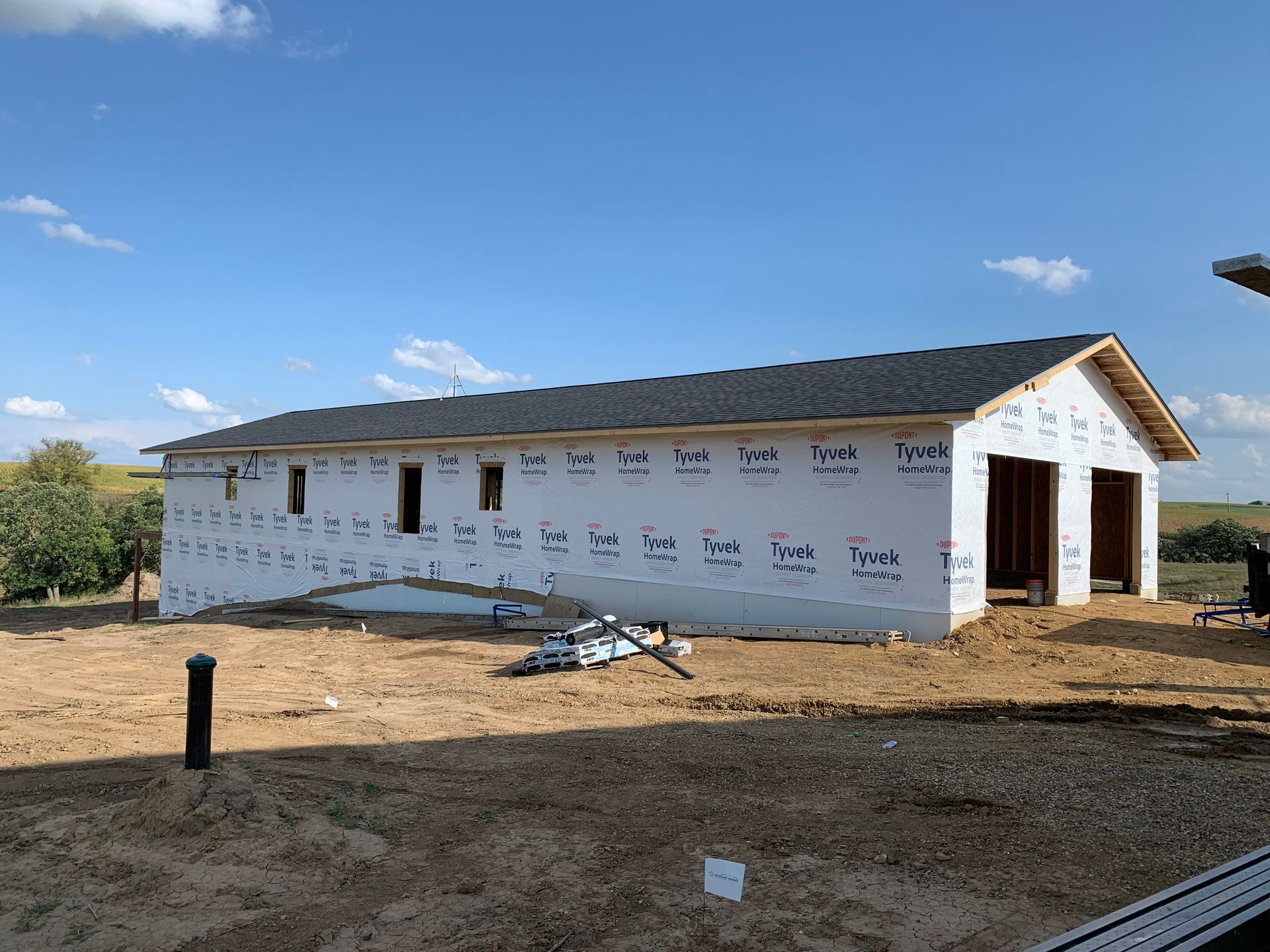 Garage under construction with a new roof, wrapped in white house wrap, on a sunny day.