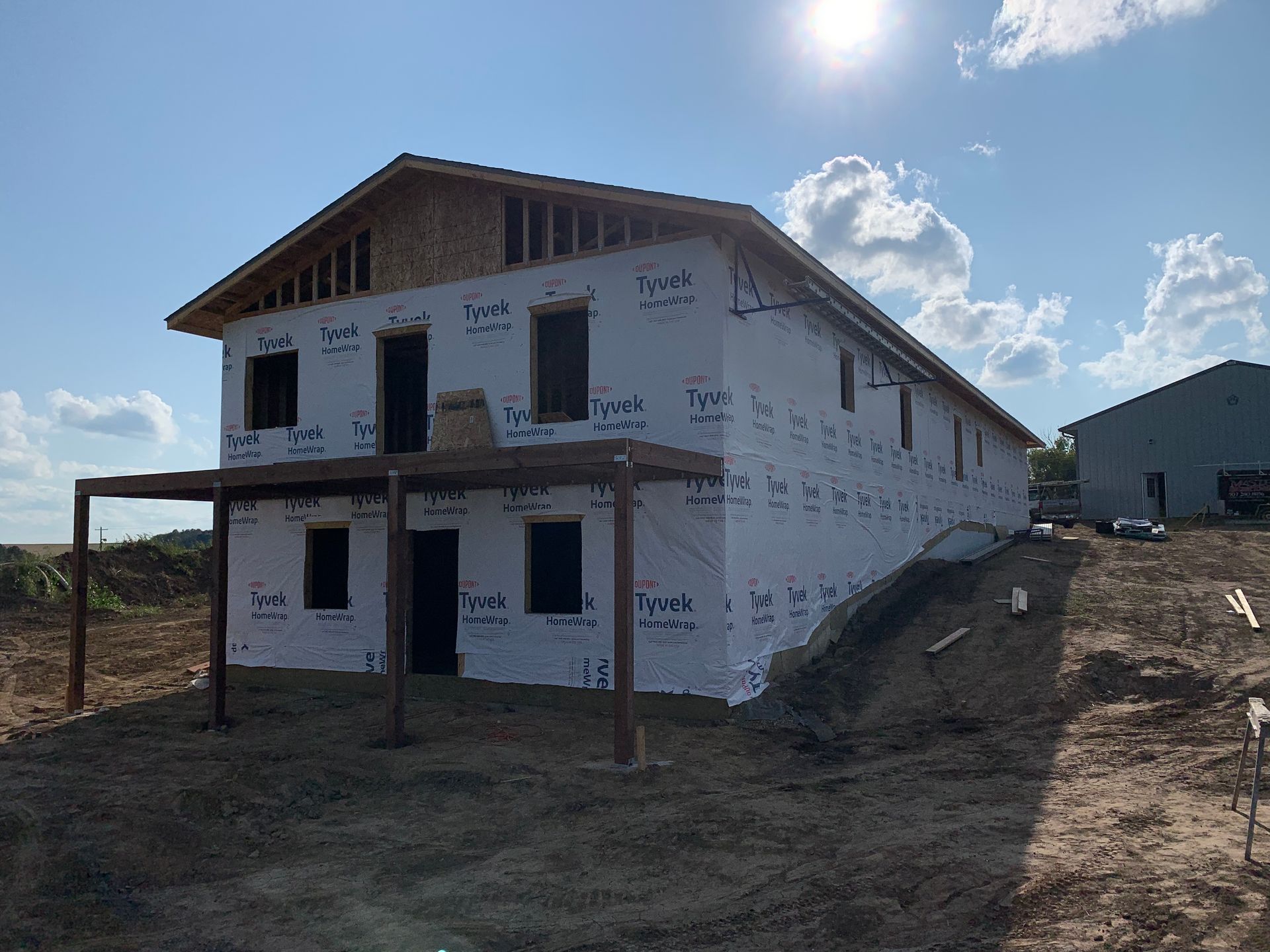 Two-story house under construction, wrapped in white, with a porch. Sunny day.