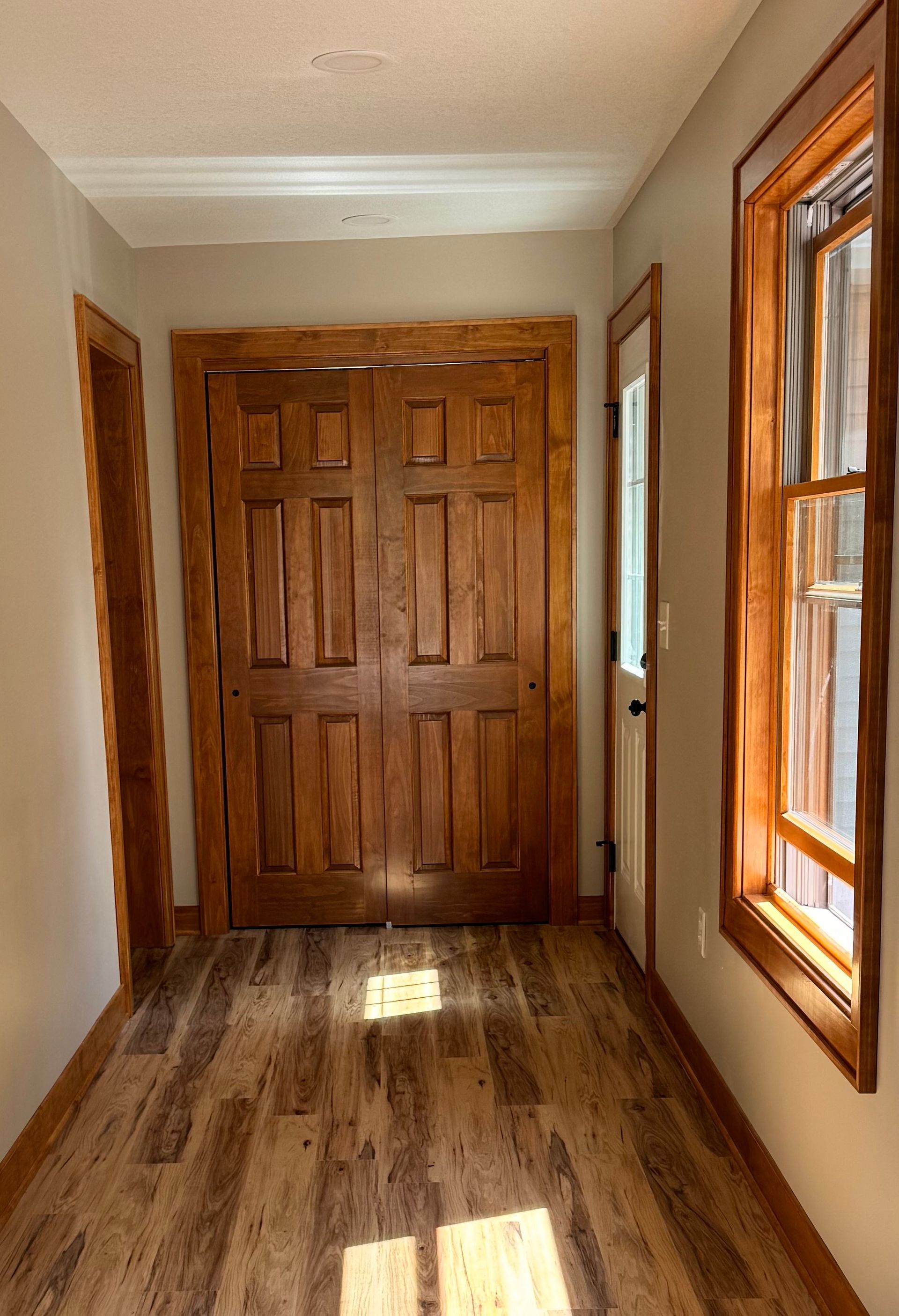 Hallway with wood doors, floors, and window frames. Natural light shines.