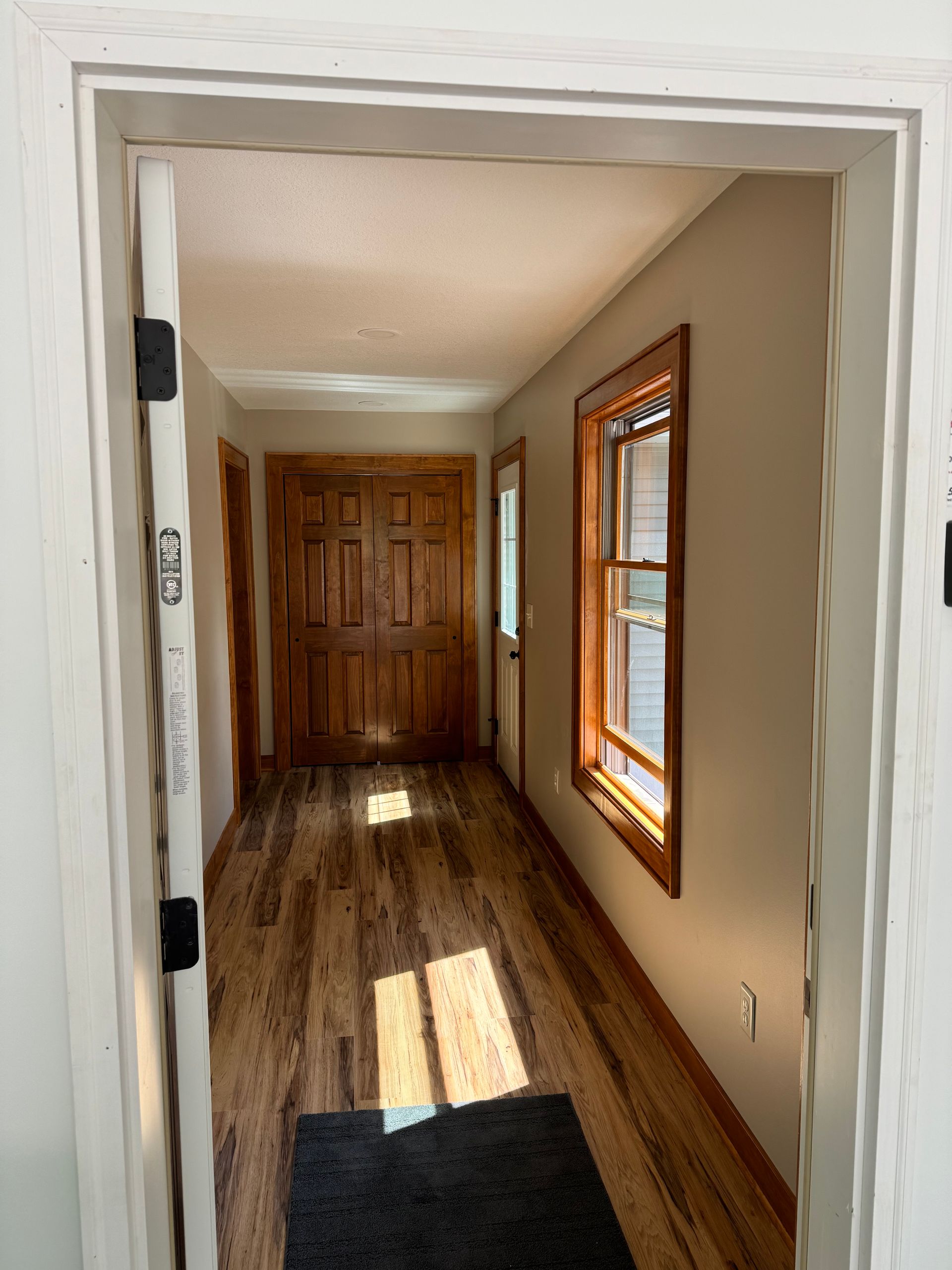 Hallway with wood floor and doors. Sunlight streams in the window.