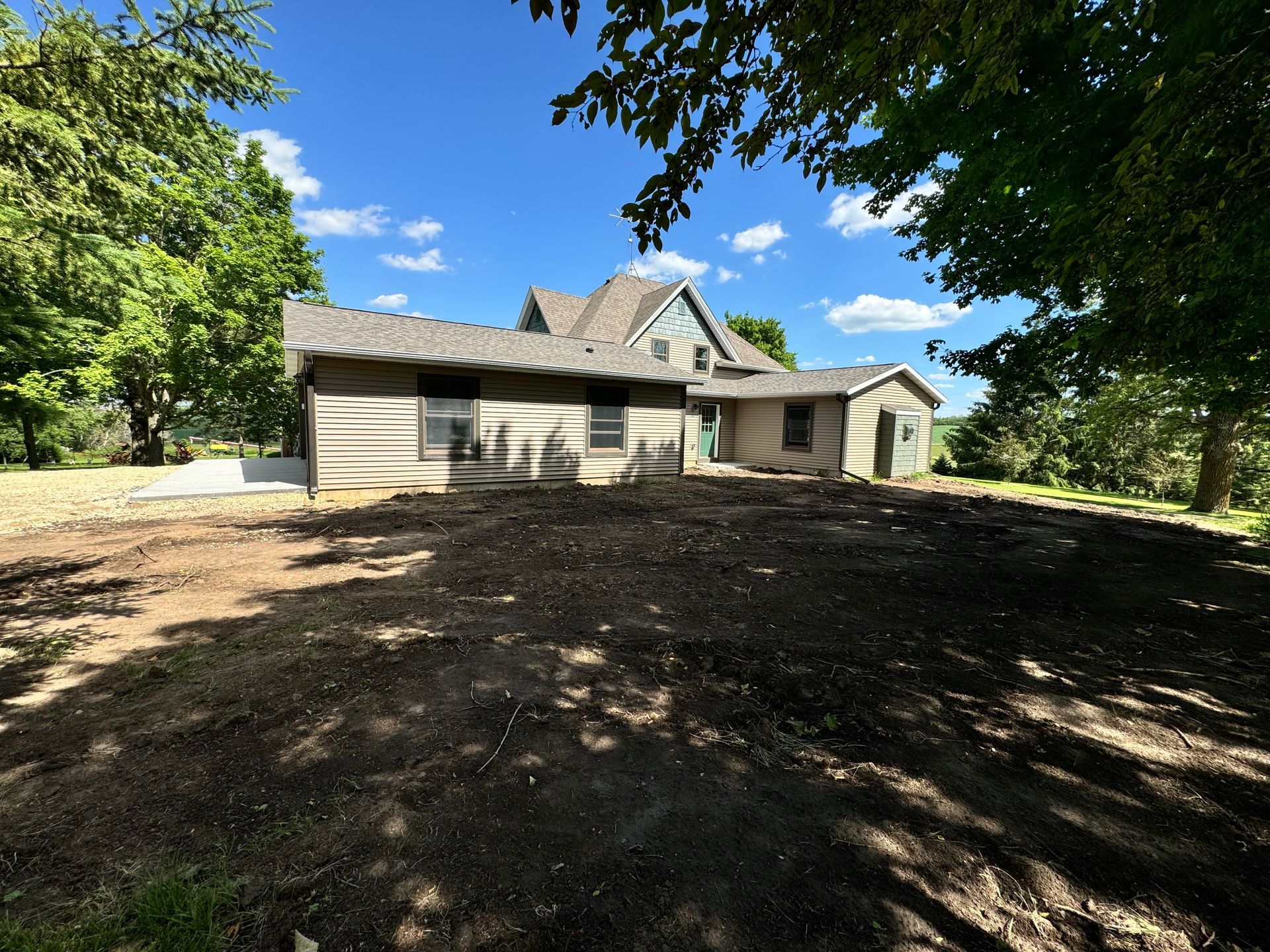 House with brown siding, dark roof, and yard of freshly tilled dark soil, under a blue sky.