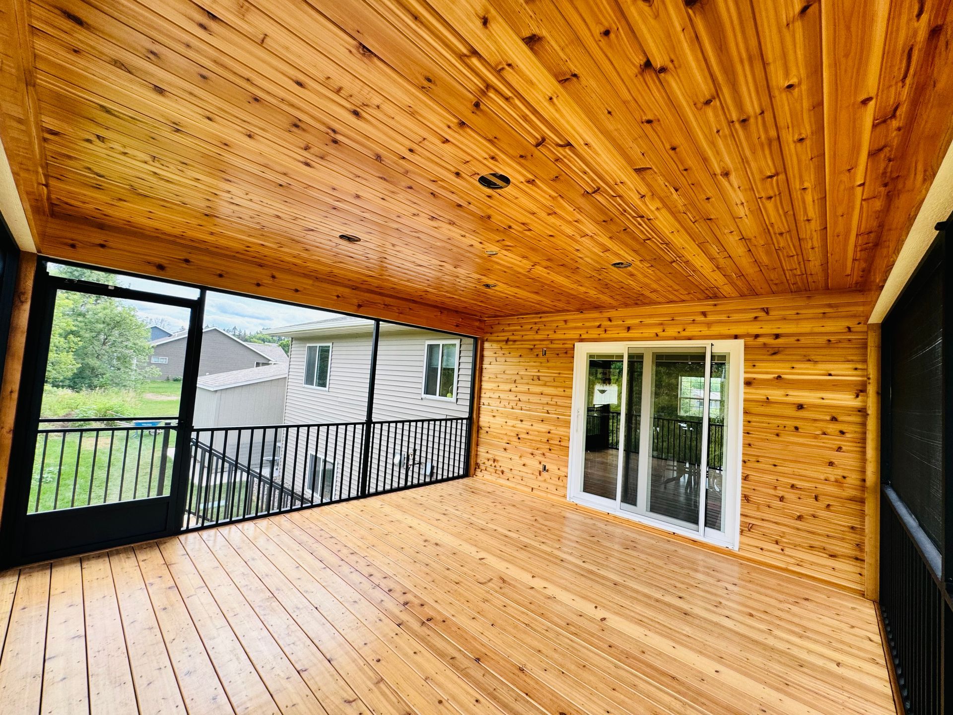 Screened porch with cedar ceiling, walls, and floor; overlooks a yard with a black railing.