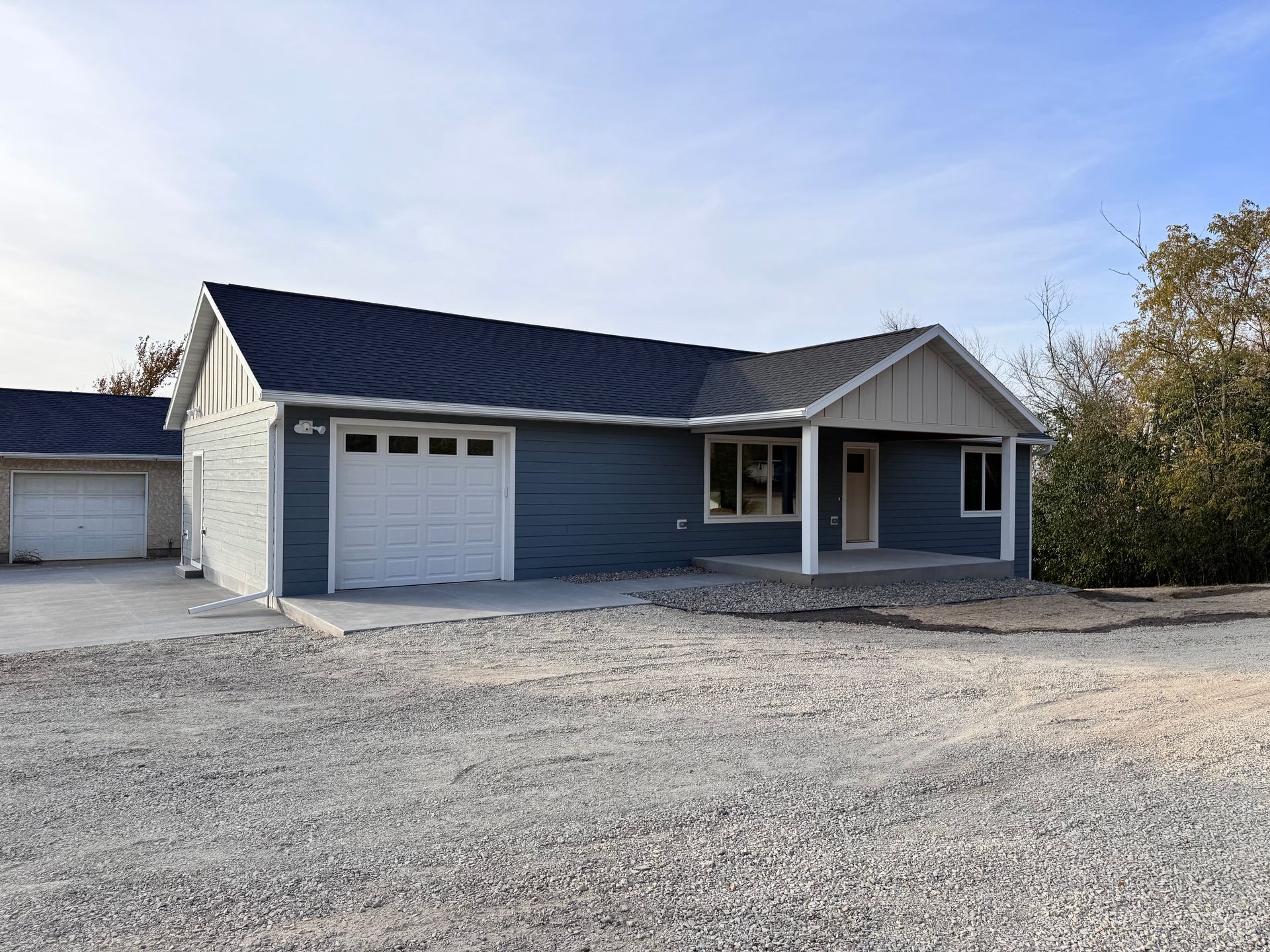 Blue house with white trim, garage, and gravel driveway on a sunny day.