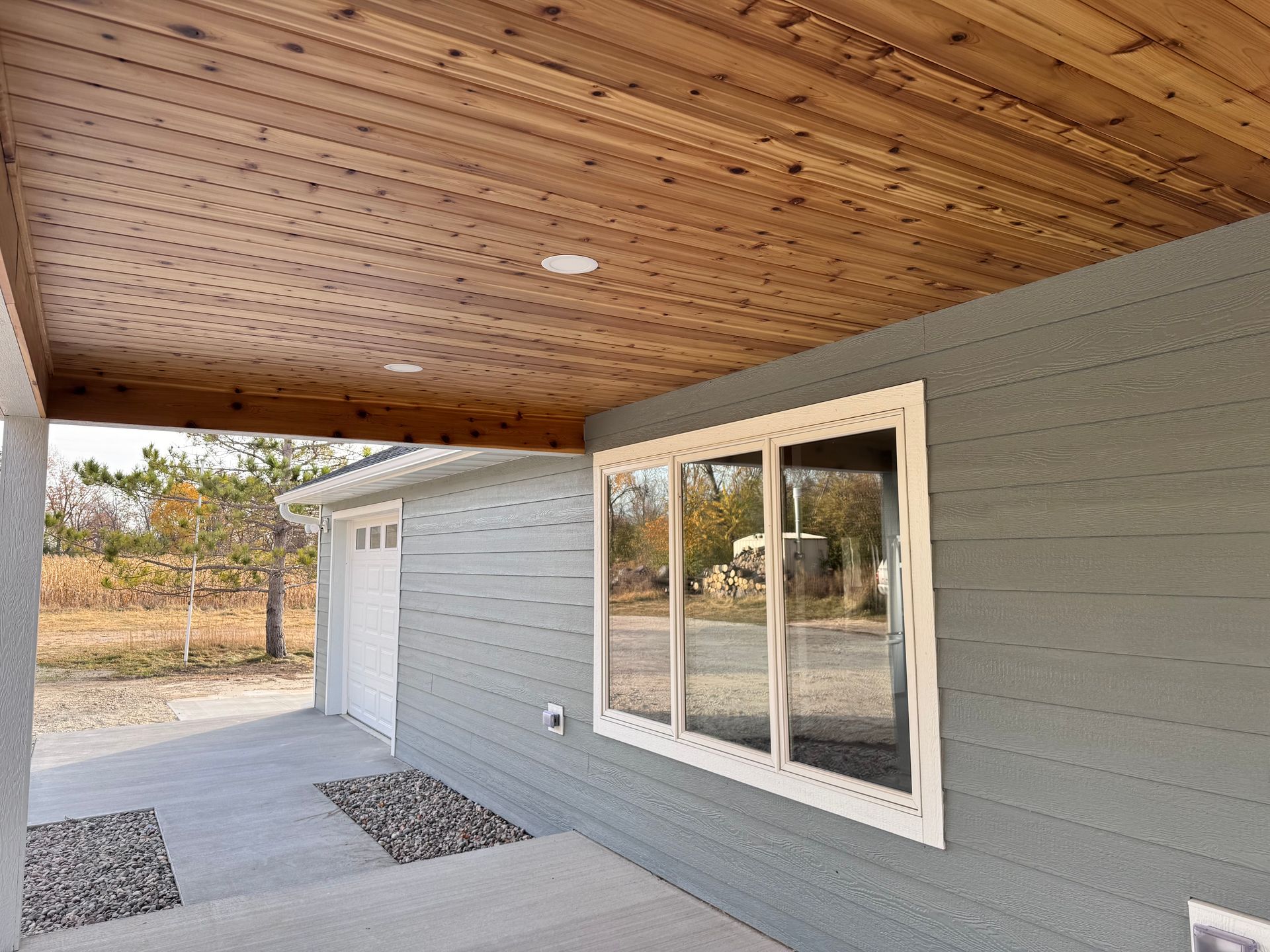 Covered porch with wood ceiling, blue siding, white window, and concrete walkway.
