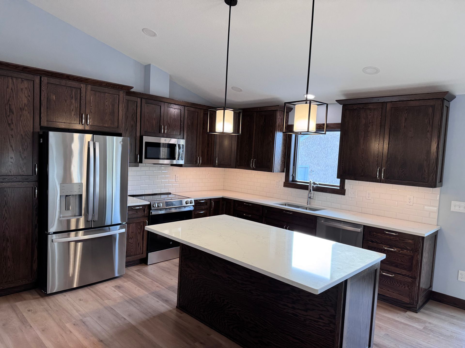 Dark wood kitchen with stainless steel appliances, white countertops, and an island.
