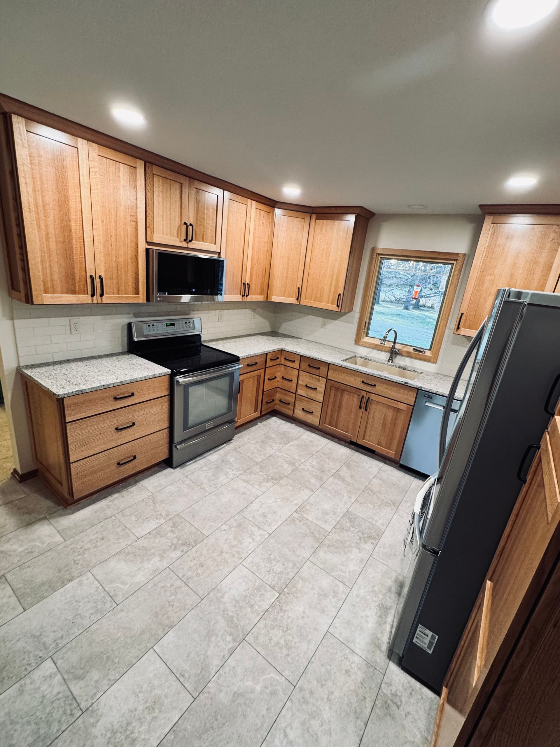 Newly renovated kitchen with light wood cabinets, stainless steel appliances, and gray tile flooring.