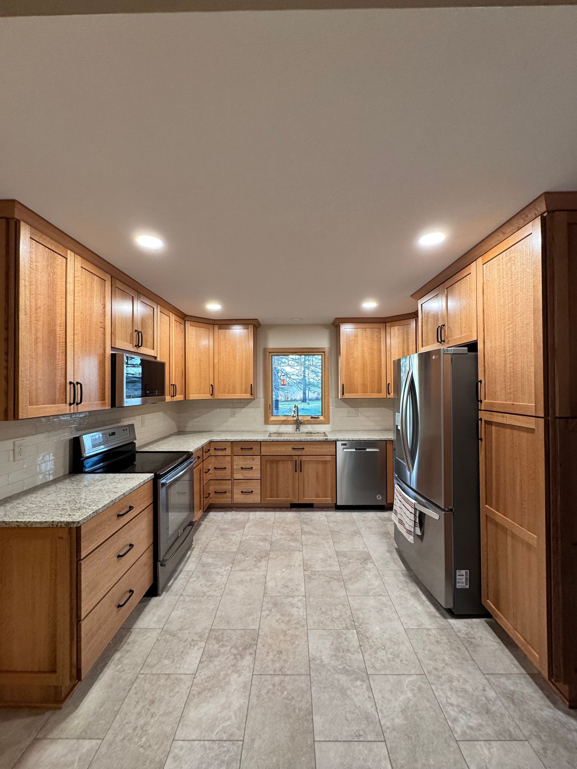 Light wood kitchen cabinets with stainless steel appliances and a window.