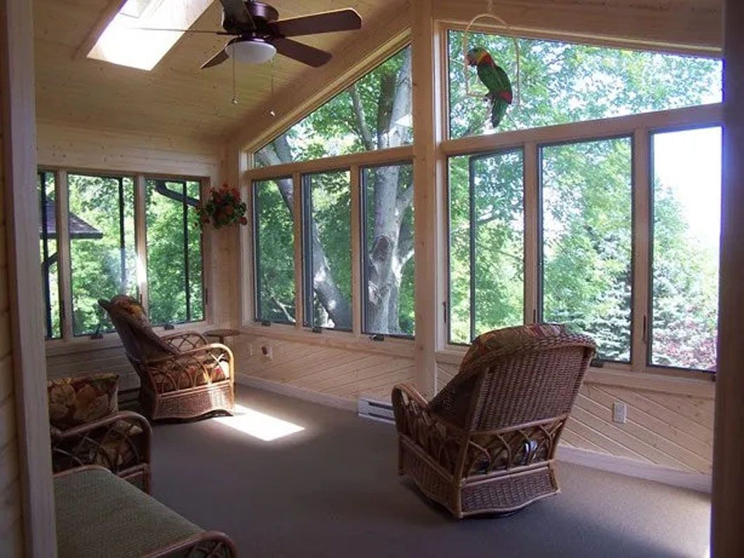 Sunroom with wicker chairs and large windows overlooking trees.
