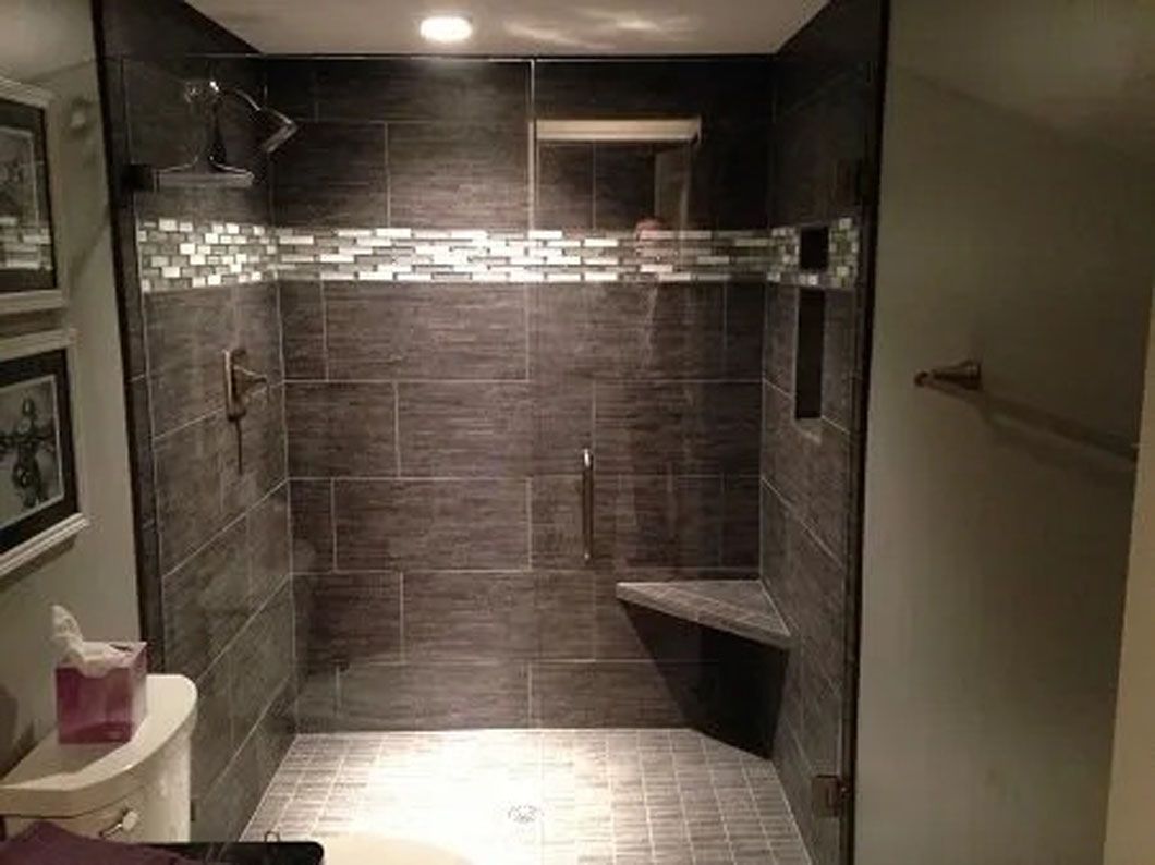 Modern bathroom shower with dark gray tile, glass door, and built-in seat.