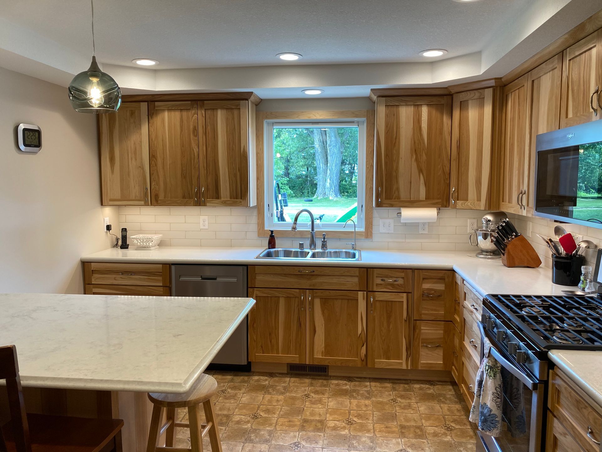 Kitchen with wood cabinets, white countertops, and a window overlooking greenery.