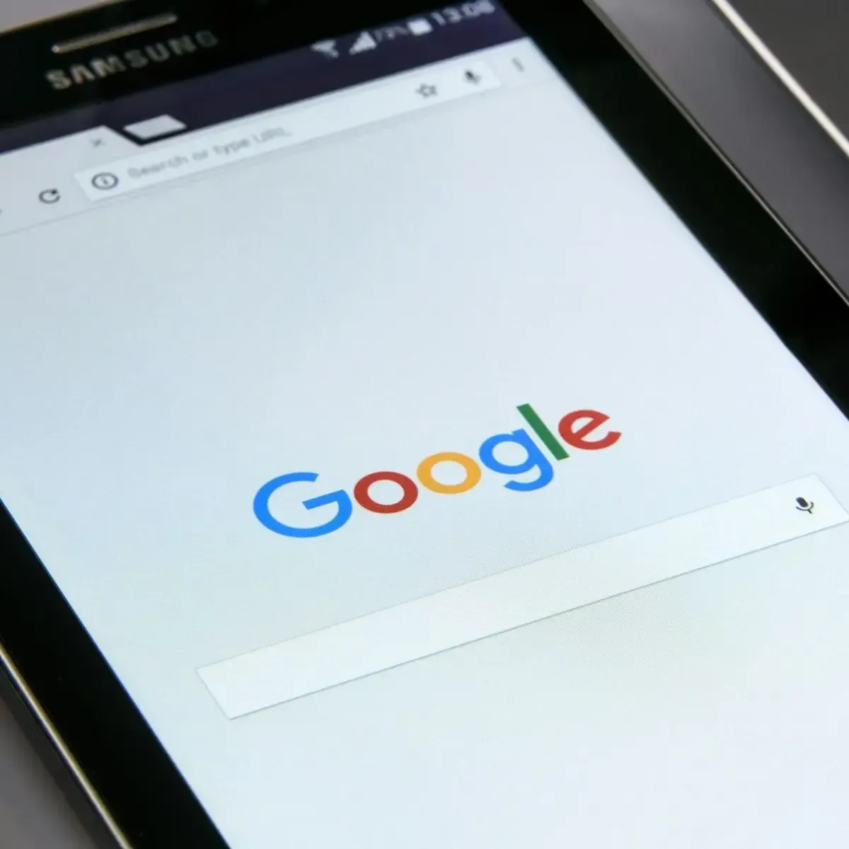 A close-up shot of a Samsung phone displaying the Google search engine homepage. 