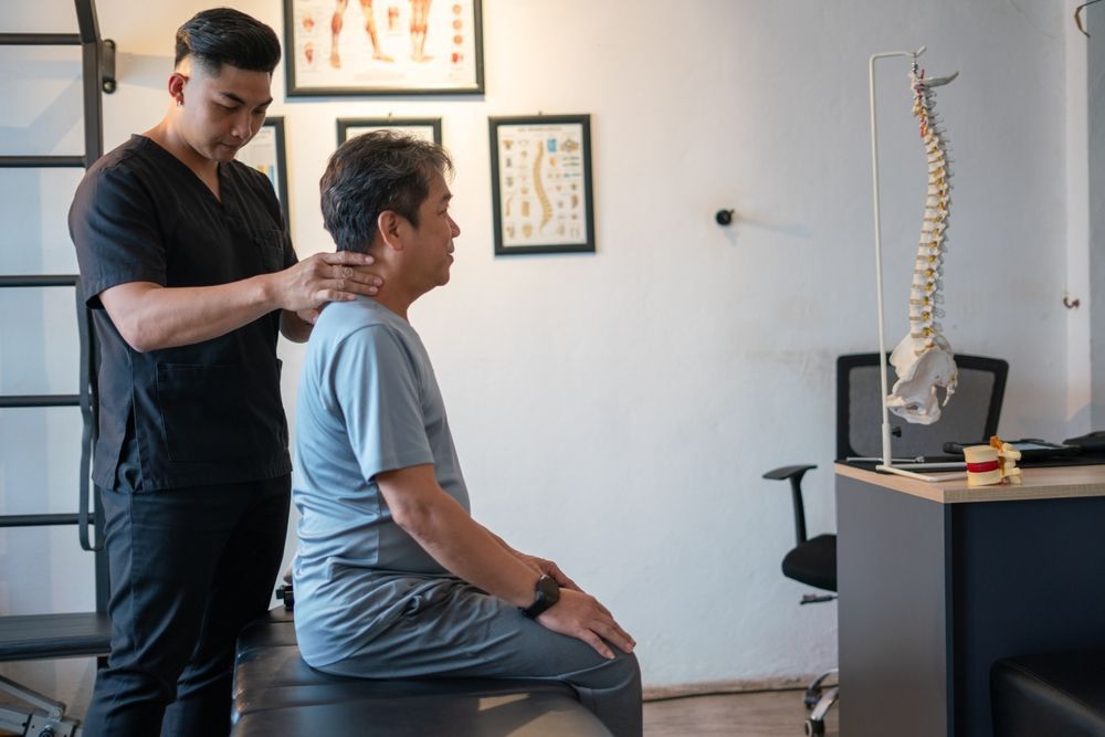 A man is sitting on a table while a doctor examines his neck.