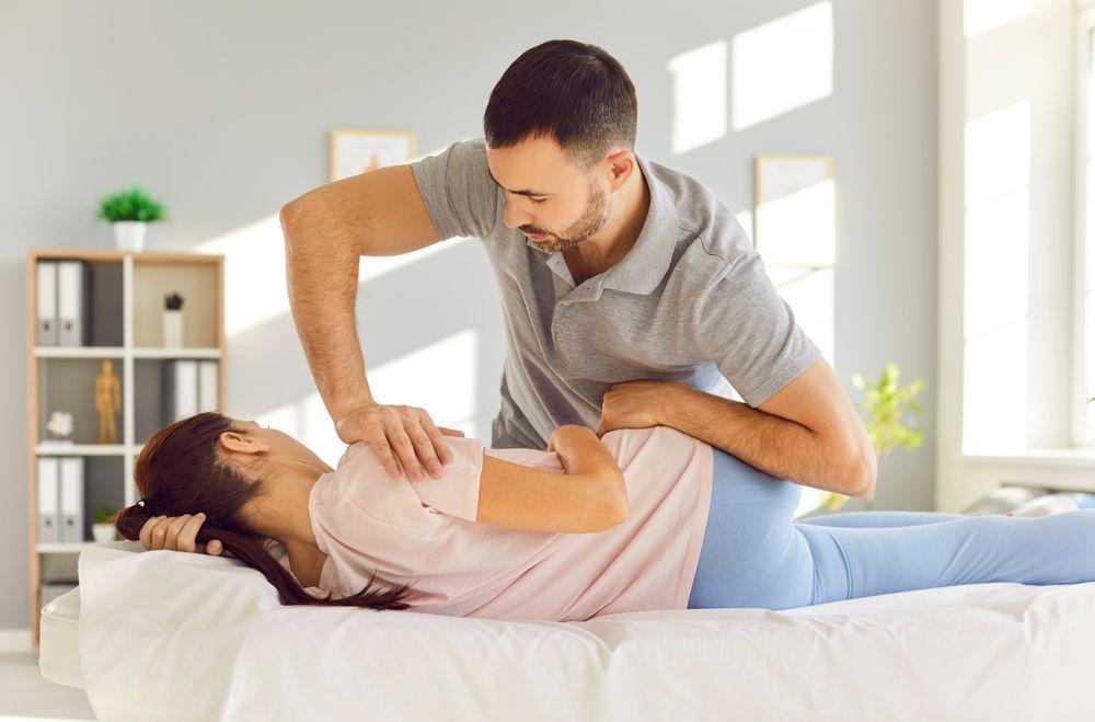 A man is stretching a woman 's back on a bed.