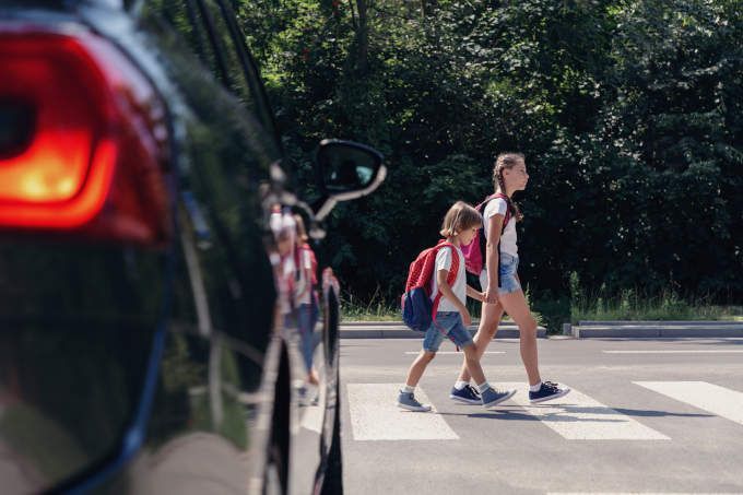 Children next to a car walking through a crosswalk on their way to school