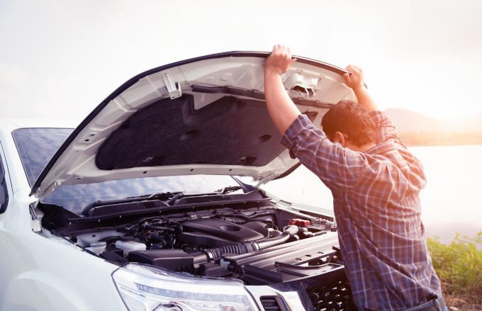 A man is opening the hood of his broken down car.