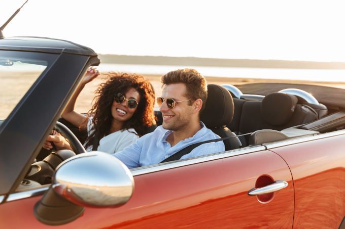 Image of a woman and man in a red convertible driving on a sunny beach