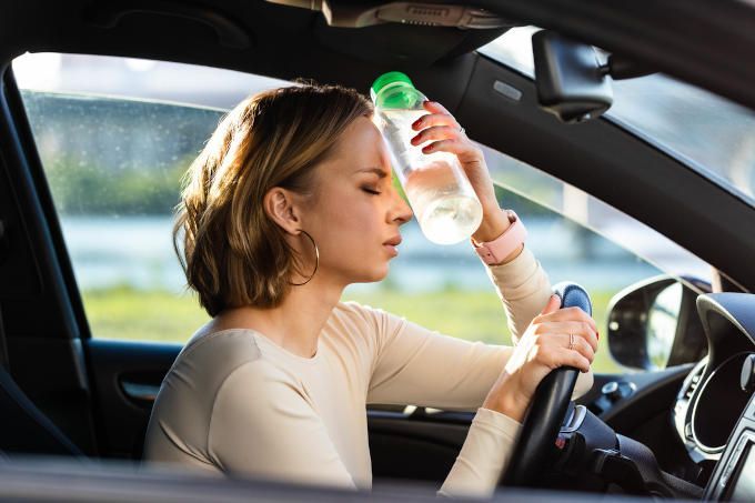 Woman in a hot car pressing a cold bottle of water to her forehead