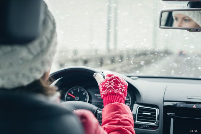 Image of inside a car with a woman dressed in winter outdoor clothing driving in snowy weather.