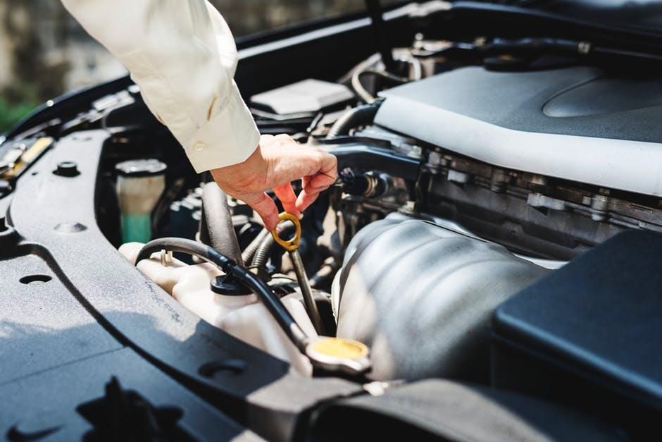 Person checking engine oil with dipstick under an open car hood