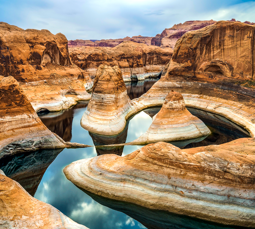 Canyon landscape with water; red rock formations and reflecting blue sky.
