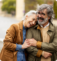 Smiling couple embracing outdoors; woman leaning on man's shoulder. They are laughing.