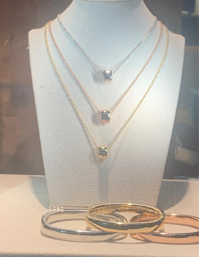 Exhibición de joyas: Collares de oro y plata con dijes, exhibidos sobre un busto blanco; pulseras de oro y plata debajo.