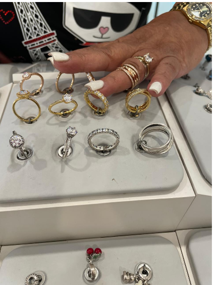 Mano señalando anillos expuestos en una bandeja blanca. Las joyas incluyen anillos de oro y plata con diamantes y otras piedras.