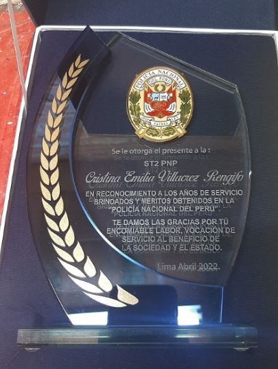 Placa en honor a “Cristina Emilia Villacreta Bengifo” con el emblema de la Policía Nacional del Perú, en vidrio y detalles metálicos.