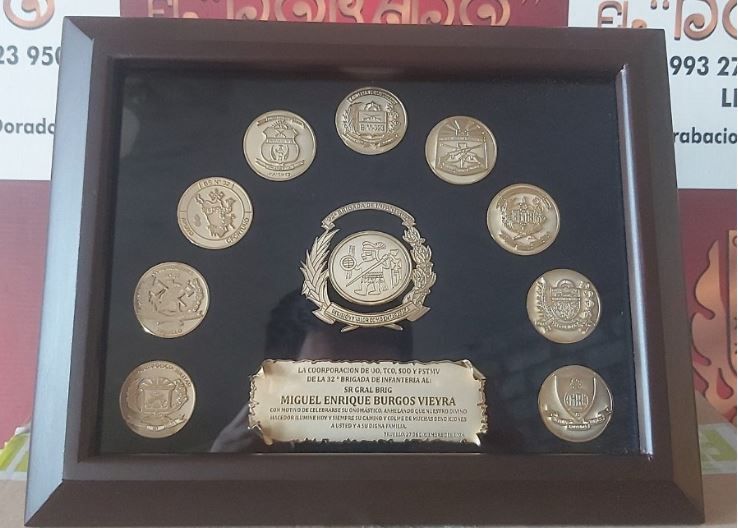 Exhibición enmarcada de monedas de oro y una placa central con texto sobre fondo oscuro.