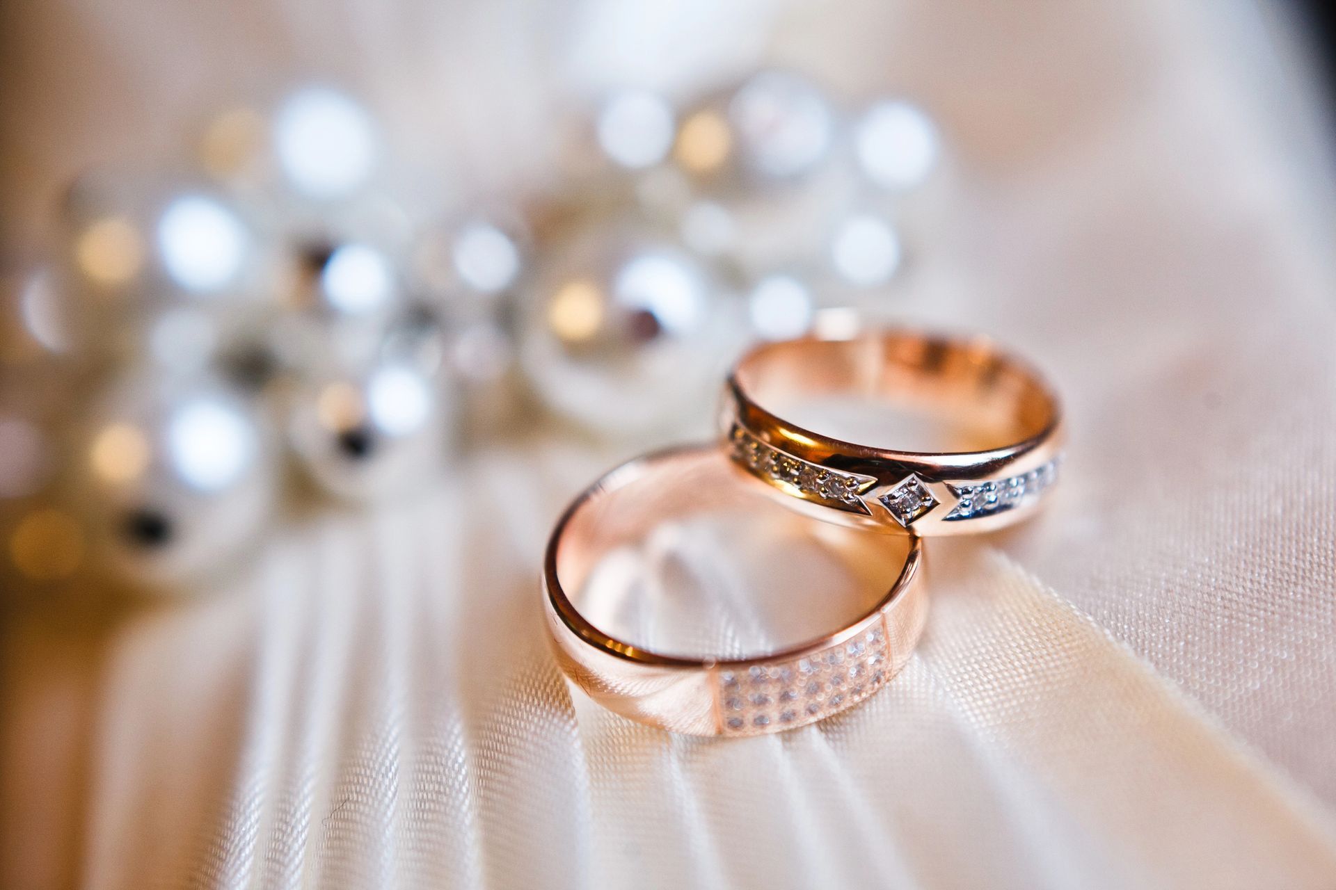 Dos anillos de boda de oro sobre satén blanco con collar de perlas de fondo.
