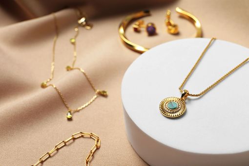 Joyas de oro sobre tela beige y plataforma blanca. Collares, pendientes y una pulsera en exposición.