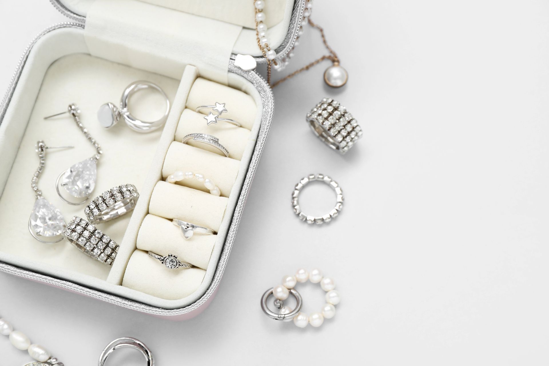 Joyero con anillos, pendientes y collares sobre superficie blanca.