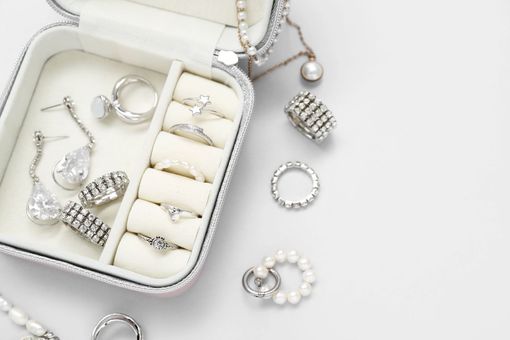 Joyero con anillos, pendientes y collares sobre superficie blanca.