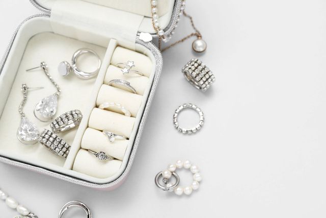 Joyero con anillos, pendientes y collares sobre superficie blanca.