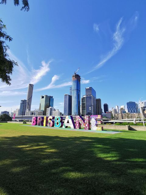 A palavra Brisbane está pintada na grama em frente ao horizonte de uma cidade.